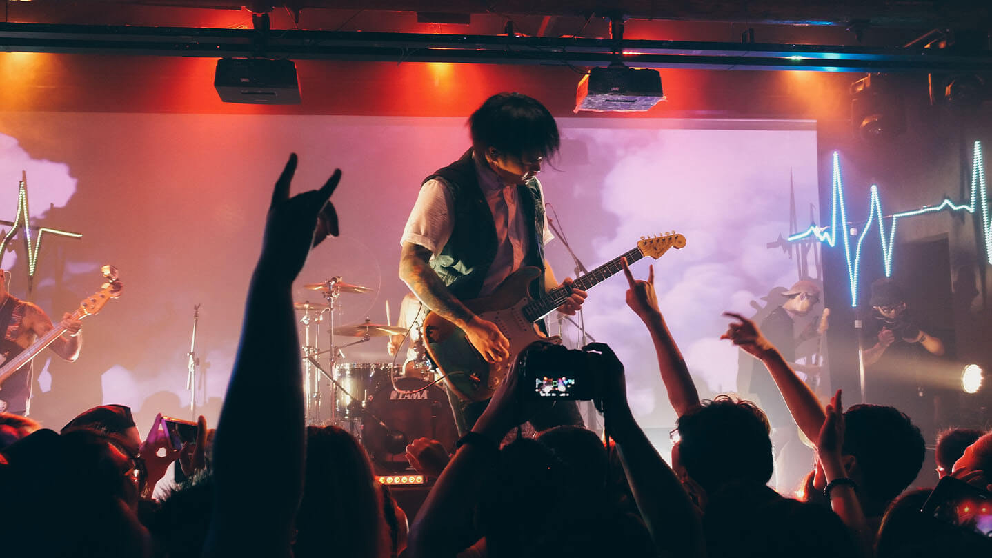 Guitarist standing on stage playing in front of a crowd with raised arms
