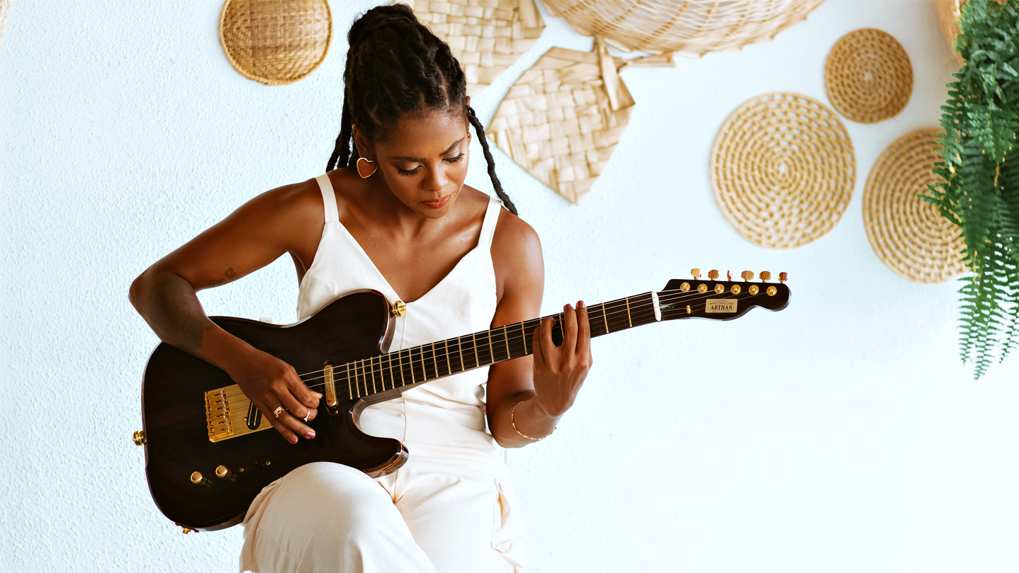 Woman seated, playing an electric guitar.