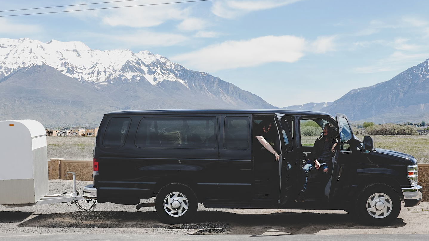 Black van with trailer, parked on the roadside with mountains in the distance