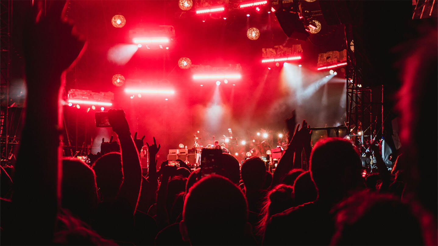 Bandzoogle blog: how to get booked at music festivals. Image of a crowd watching a band perform on a festival stage at night, view from within the crowd of people.