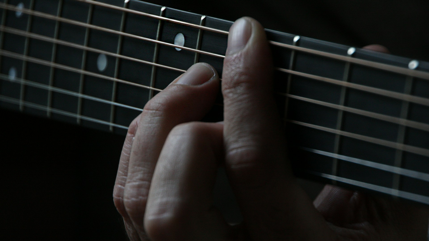 Bandzoogle blog: freshen up your songwriting with borrowed chords. Image of a hand fretting a chord on an acoustic guitar.